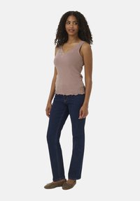 Débardeur rose clair à côtes avec un ourlet en dentelle, associé à un jean droit bleu foncé et des chaussures plates marron.