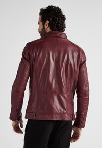 Burgunderfarbene Lederjacke mit strukturiertem Design, gesteppte Schulter- und Ärmelakzente sowie Reißverschlusstaschen für einen taillierten Look.