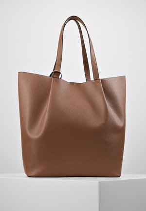 Brązowa skórzana torba typu tote z dwoma długimi rączkami, gładką fakturą i subtelnymi przeszyciami, prezentowana na białym podeście na tle jednolitego tła.