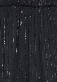 Tissu noir plissé avec des fils argentés verticaux scintillants et une ceinture élastique.