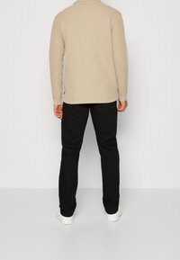 Top beige texturizado de manga larga con cuello redondo, combinado con pantalones negros y zapatillas blancas. Vista desde la parte de atrás.