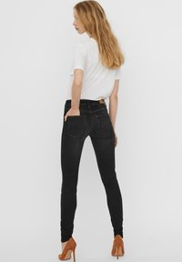 Crne skinny traperice s dva stražnja džepa, visokim strukom i glatkom teksturom. Uparene s bijelom majicom i smeškim potpeticama.
