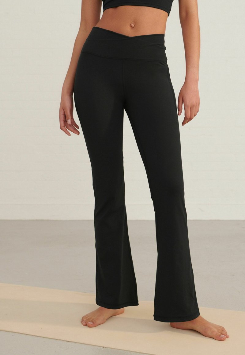Pantalons de yoga noirs avec un ourlet évasé, fabriqués en tissu extensible, dotés d'une large taille pour plus de confort. Surface texturée sans motifs.