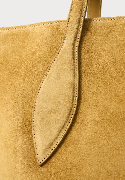 Sac fourre-tout en daim jaune avec une finition lisse et texturée, présentant des poignées allongées et des coutures détaillées le long des bords.