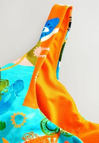 Kleurige zwemkleding heeft een levendige blauwe en oranje stof met abstracte patronen en texturen. De bandjes zijn strak en het materiaal lijkt glad.