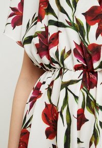 Vestido floral con una base blanca y estampado botánico en rojo y verde, cintura fruncida, tejido ligero y acabado suave y texturizado.