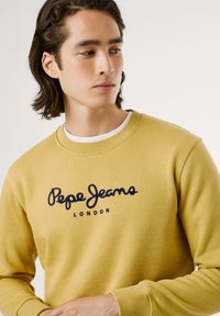 Felpa gialla in cotone con scollo rotondo, dotata di logo del brand ricamato in blu navy "Pepe Jeans LONDON" sulla parte anteriore.