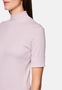 Light pink, short-sleeve turtleneck top with a fitted design and rolled cuffs, made from a smooth, stretchy fabric.
