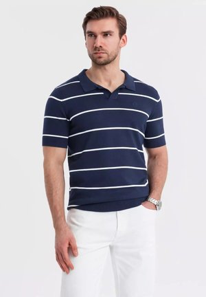 Marineblaues kurzärmliges Poloshirt mit weißen horizontalen Streifen, ausgestattet mit einem Kragen und gerippter Textur. Getragen mit weißen Hosen und einer Uhr.