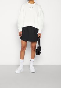 Vit sweatshirt med en svart Nike-logga, ihopparad med en svart kjol, vita strumpor och vita sneakers. Accessoar är en liten svart väska.