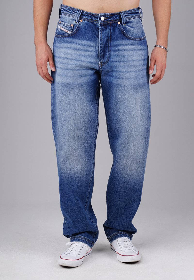 Hellblaue Jeans aus Denim mit lockerer Passform, verblasster Textur, Fünf-Taschen-Design und Kupferriegeln, kombiniert mit weißen Sneakers.