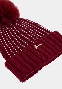 Beanie a maglia borgogna decorato con borchie trasparenti, dotato di un pompon soffice sulla cima e una manica a coste con un accento di logo dorato.