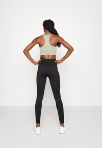 Sportbehå i ljus beige med racerback-design, i kombination med hög midja svarta leggings, båda gjorda av elastiskt tyg. Vita sneakers fulländar looken.