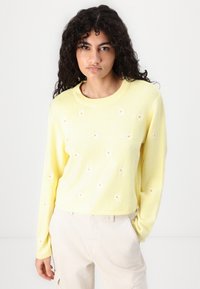 Gul stickad tröja med rund krage och långa ärmar, med vit blomsterbroderi över framsidan. Mjuk textur, kort design.