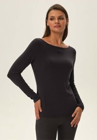 Schwarzes Langarmoberteil mit weitem Ausschnitt, glatter Textur, taillierter Passform und nahtloser Konstruktion, kombiniert mit dunkel gerippten Leggings.