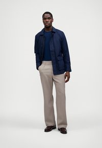 Marineblauer leichter Blazer über einem blauen T-Shirt, kombiniert mit beigen karierten Hosen und braunen Schuhen. Reduziertes Design mit praktischen Taschen.