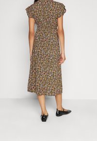 Abito midi floreale con maniche corte a sbuffo; sfondo nero con piccoli fiori colorati. Il modello indossa scarpe nere flat.