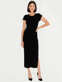 Czarna, prążkowana sukienka midi z krótkimi rękawami, rozcięciem po boku i okrągłym dekoltem. Gładka tekstura, dopasowany krój, zestawiona z czarnymi szpilkami.