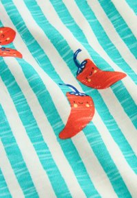 Modrobielo pruhovaná látka s potlačou červených chilli papričiek so usmievavými tvárami a zelenými stonkami.