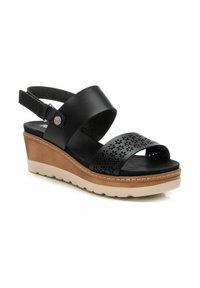 Sandalia cuña negra de cuero con diseño perforado, correa ajustable y suela beis. Cuenta con una plantilla texturizada y acolchada.