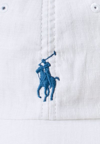 Witte stoffen pet met een blauw geborduurd logo van een polo-speler en paard, met zichtbare stikdetails en oogjes voor ventilatie.