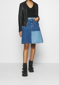 Denimrock mit zweifarbigem Design, der dunkle und helle blaue Panels aufweist. Kombiniert mit einer schwarzen Lederjacke und schwarzen Schnallenstiefeln.