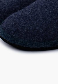 Granatowe filcowe kapcie z zaokrąglonym czubkiem, teksturowaną powierzchnią i kontrastującą czarną podeszwą. Miękki, gruby materiał zapewniający komfort i ciepło.