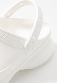 Vit sandal med en texturerad rem med perforeringar, slät gummikropp och en något upphöjd sula för komfort.