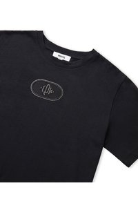 Camiseta de algodón negra con cuello redondo y mangas cortas. Presenta un parche decorativo de malla con rhinestones en el centro.