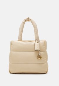 Beżowa pikowana torba na ramię z dwoma uchwytami, o prostokątnym kształcie, gładkiej fakturze i złotym ozdobnym elementem.