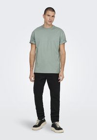 Lichtgroene katoenen T-shirt met opgerolde mouwen, gecombineerd met zwarte broeken en zwarte sneakers met een dikke witte zool.