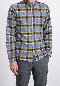 Langsleevige blouse met een blauw, geel en grijs ruitpatroon. Gemaakt van een textuurstof met een standaard kraag en knopen.