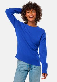 Pull-over bleu royal avec un col rond, des manches longues et un ourlet côtelé. Texture douce avec une coupe légèrement décontractée, associé à un jean en denim.