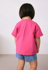 T-shirt en coton rose vif à manches courtes, coupe décontractée et encolure arrondie, associé à un short en denim. Vue centrée de dos.