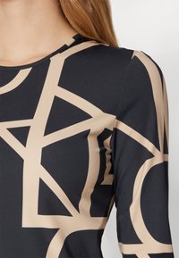 Langermet topp med et geometrisk mønster i beige på en mørk marineblå bakgrunn. Laget av glatt, elastisk stoff med rund hals.
