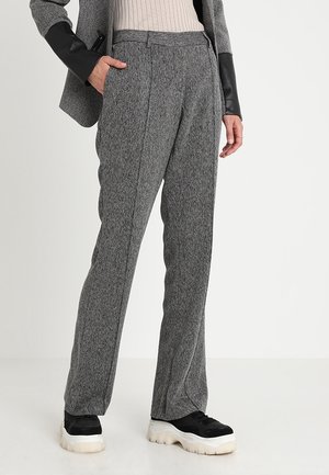 Pantalon texturé gris à coupe ajustée, avec une taille mi-haute et des plis sur le devant ; associé à des baskets noires.