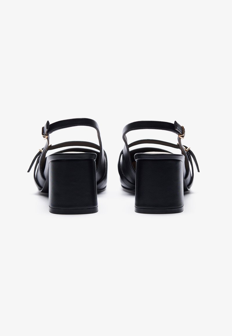 Sandales en cuir noir avec un talon bloc. Elles comportent une lanière de cheville avec une boucle et des lanières fines sur le pied, texture lisse, design simple.