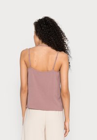 Camisole en satin rose poudré avec fines bretelles ajustables, présentant une surface texturée et une coupe décontractée, dévoilant le dos.