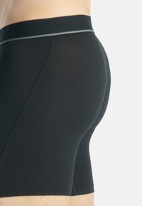 Svarta boxershorts tillverkade av ett slätt, elastiskt material. Har en ribbad midja med en kontrasterande grå detalj och sid sömmar.