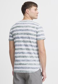 T-shirt rayé blanc, avec des rayures horizontales vertes et bleues. Manches courtes, col rond et ourlet légèrement courbé à l'arrière.