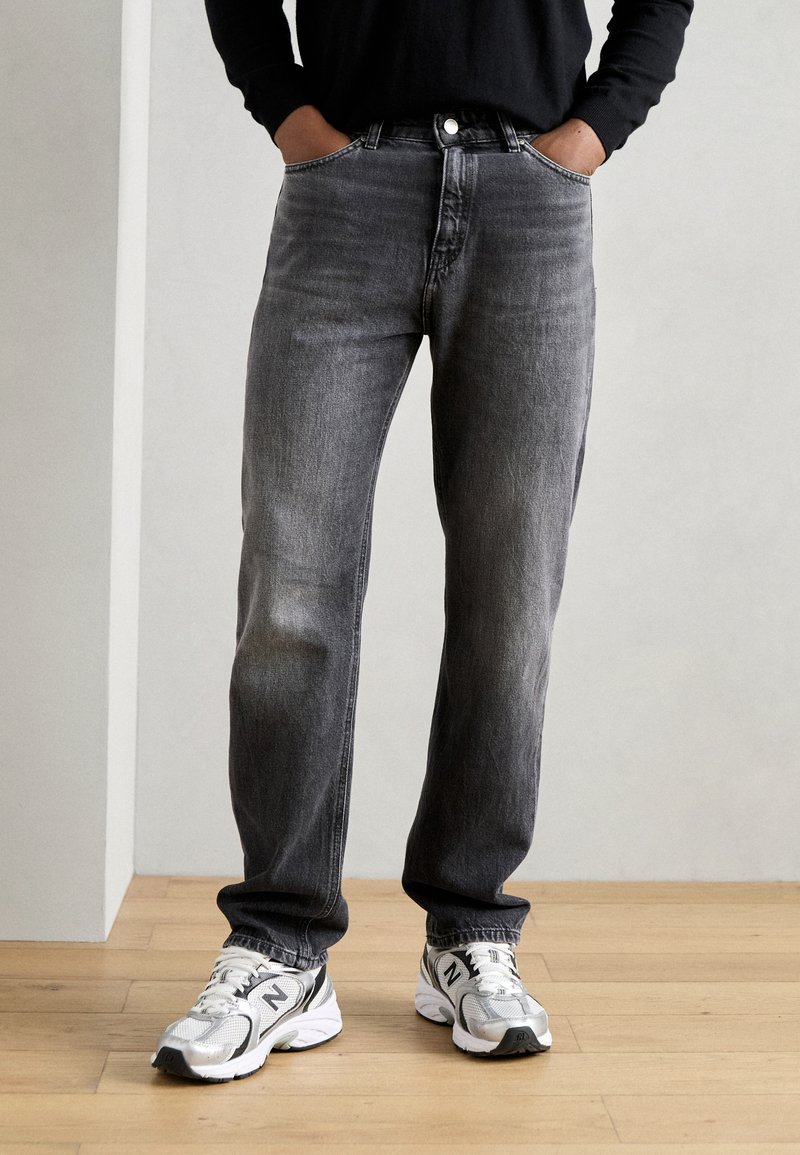 Mørkegrå denimjeans med avslappet passform, femlommers design og frontknapping, kombinert med grå og hvite treningssko.