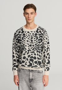 Maglione lavorato a maglia nero e crema con design a stampa leopardata, scollo rotondo e polsini e orlo a coste. Abbinato a jeans grigio chiaro.