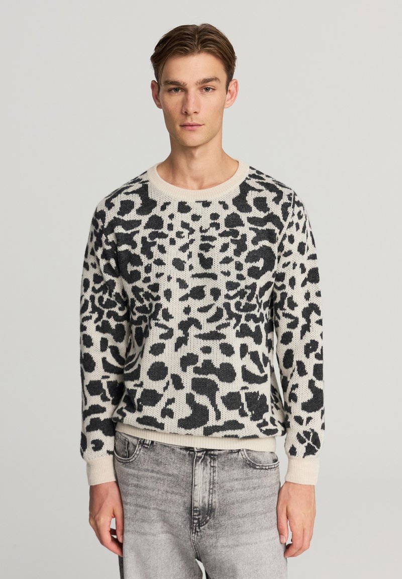 Maglione lavorato a maglia nero e crema con design a stampa leopardata, scollo rotondo e polsini e orlo a coste. Abbinato a jeans grigio chiaro.
