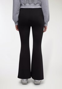 Pantaloni neri a zampa realizzati in materiale morbido ed elastico, con vita alta e una trama liscia e opaca. Indossati con una felpa grigia corta.