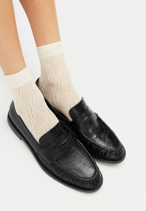 Černé kožené mokasíny s hladkým povrchem, dekorativním prošitím a třásněmi, doplněné o lehké vzorované kotníkové ponožky.