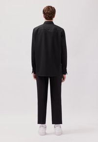 Schwarzes Langarmshirt mit geradem Schnitt, kombiniert mit schwarzen Hosen und weißen Sneakers. Glatter Stoff, minimalistisches Design und knöpfbare Manschetten.