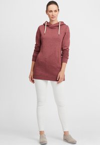 Sweat à capuche bordeaux avec un col cheminée, des manches longues et des cordons de serrage. Dispose de poches kangourou et d'accents marron sur les côtés.