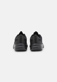 Chaussures de sport noires avec une tige en maille respirante, des détails texturés et une semelle coussinée. Elles comportent une languette à la talon pour un enfilage facile.