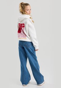 White hoodie with red and pink graphic text on the back, paired with blue wide-leg jeans. Smooth cotton fabric, casual fit.
