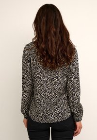 Chemise noire à manches longues avec un petit motif floral beige. Présente une patte de boutonnage et des poignets ajustés. Tissu lisse et léger.